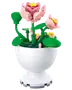 LEGO-liknande rosa blommor med gröna stjälkar och blad i en vit dekorativ vas.