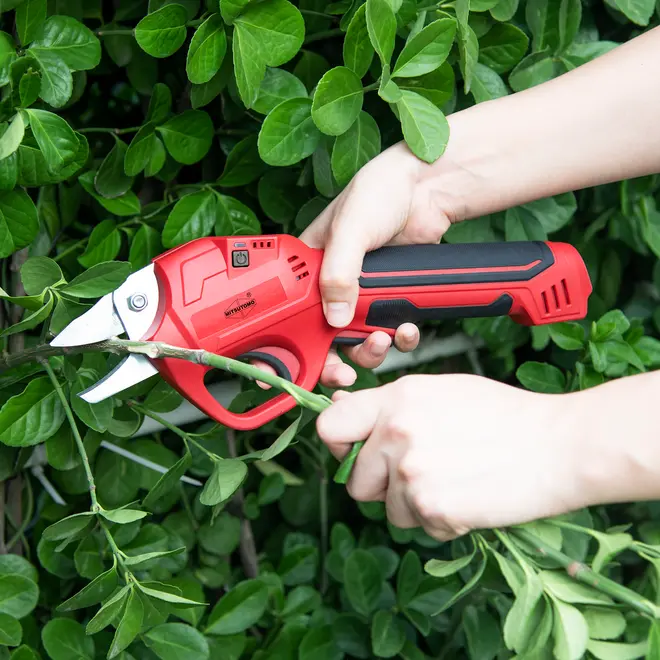 Röd elektrisk sekatör med ergonomiskt svart handtag, avsedd för att klippa grenar och stjälkar. Utrustad med avtryckare och vassa metallblad, perfekt för trädgårdsarbete.