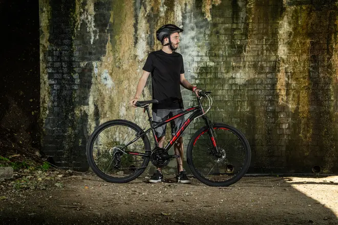 Sort og rød mountainbike med frontaffjedring, skivebremser, grove dæk og let stel. Velegnet til terrænkørsel. Vises med rytter iført hjelm og afslappet tøj.