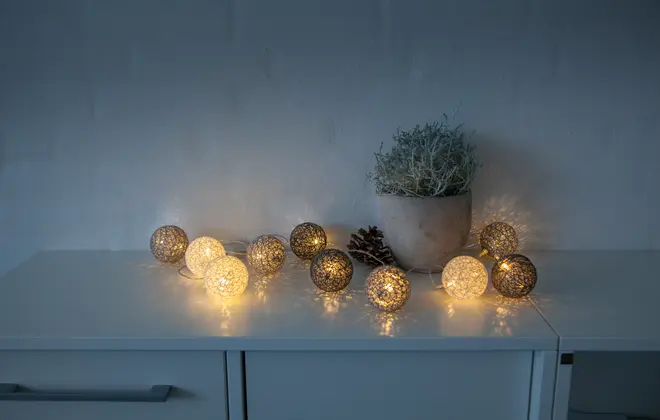 Ljusslinga med dekorativa LED-bollar i varmvit och guld, placerad på vit byrå. Perfekt för heminredning, festlig stämning eller mysig belysning.