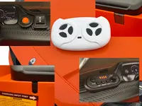 Nærbillede af orange elbil-legetøj med kontrolpanel, fjernbetjening, opladningsport og musikpanel med forskellige funktionsknapper og indikatorlys.