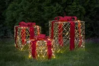 Set med tre utomhusbelysta presentaskar med guldfärgade trådramar, röda glitterband och rosetter. Varje ask är upplyst med varmvita LED-lampor för festlig dekoration.