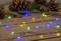 Slinga med flerfärgade LED-lampor i grönt, blått, gult och rött på tunn tråd, perfekt för dekoration. Kottar och grankvistar i bakgrunden.