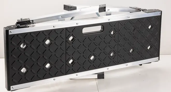 Sammenklappelig arbejdsplatform med sort, mønstret overflade og integreret håndtag. Fremstillet af metal og plast, kompakt til nem transport og opbevaring. Velegnet til gør-det-selv.