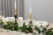 Festligt bordpynt med grønne grangrene, guldkugler, kogler, hvide stearinlys og glas. Navnekort og servietter med juletema fuldender det elegante julebord.
