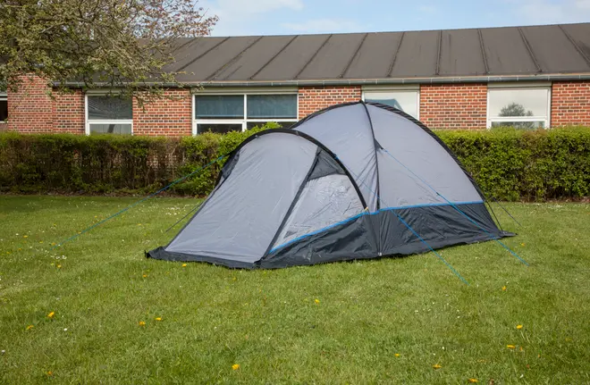Grå og sort kuppeltelt med to rum, vandtæt materiale, netvinduer og blå barduner, opslået på græs. Passer til 2-4 personer, ideelt til camping eller udendørs brug.