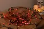 Slinga med röda LED-Halloweenlampor och svart sladd, placerad på en träyta. Dekorativ dödskalle-ljushållare med tända ljus syns i bakgrunden.