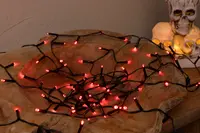 Slinga med röda LED-Halloweenlampor och svart sladd, placerad på en träyta. Dekorativ dödskalle-ljushållare med tända ljus syns i bakgrunden.