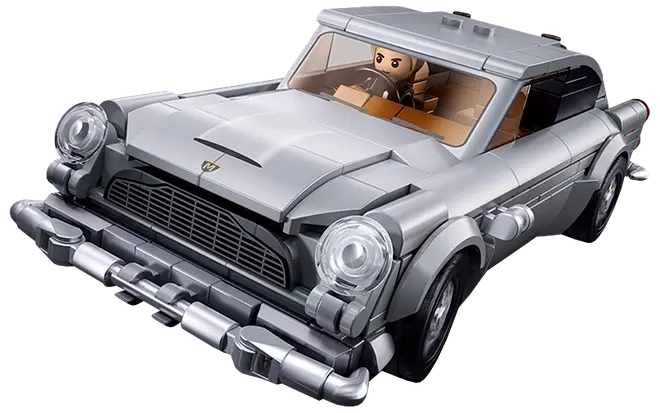Silverfärgad leksaksbil i vintagestil med runda strålkastare, kromdetaljer, svart grill, beige interiör och en minifigur vid ratten.