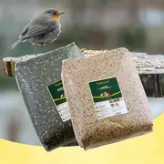 To store forseglede poser fuglefoder, én med mørke solsikkekerner og én med lyse frøblandinger, vist med en rødhals på et foderbord.