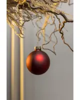 Matt röd julgranskula med guldfärgad topp, hängande i tunn guldsnöre. Enkel och klassisk dekoration för julgran eller hemmet.