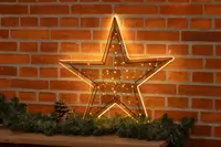 Upplyst stjärnformad dekoration med varmvita LED-lampor, metallram och ljusslinga. Passar för inomhusjuldekoration, visas mot tegelvägg med grangirlang.