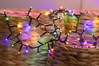A string of multicolored LED lights with small bulbs is draped over woven, natural-colored baskets. The lights feature red, green, blue, yellow, and purple colors, and the wire is black. The baskets have a textured, braided pattern and a cylindrical shape.