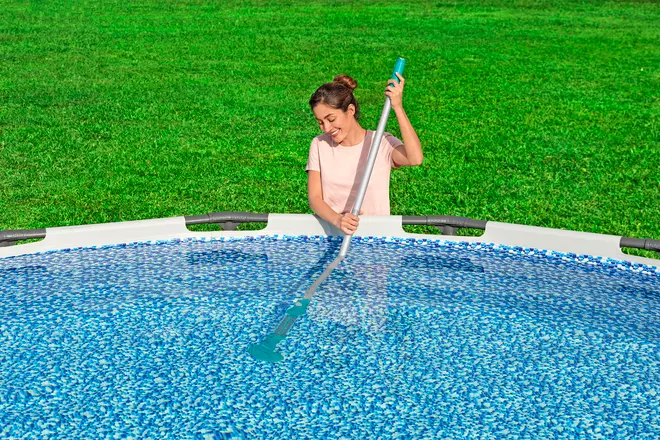 Rund fritstående pool med blå mosaikmønster, solid hvid ramme og person, der bruger langt skaft til rengøring. Perfekt til baghaven og nem vedligeholdelse.
