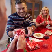 Rektangulær gaveæske med rød og hvid stribet gavepapir og rød båndsløjfe, udveksles ved et festligt bord med mad og drikke.