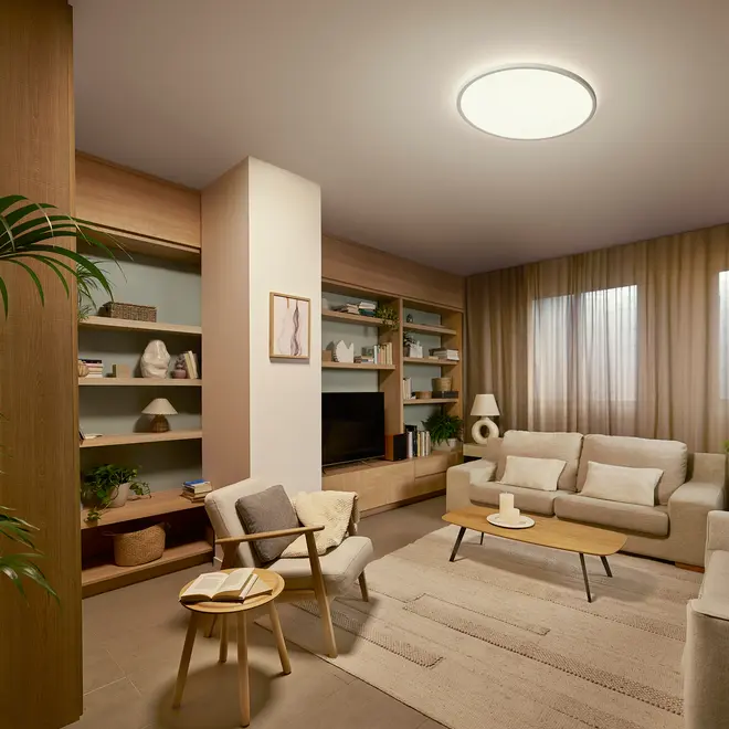 Moderne stue med beige sofaer, træbord, bogreoler, neutrale dekorationer, stor loftslampe og gardiner. Hyggeligt siddeområde med lænestol, sidebord og dekorative elementer.