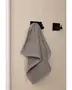 Gråt håndklæde hænger på en moderne sort vægkrog, tekstureret beige væg. Håndklædet ser blødt og absorberende ud, ideelt til badeværelse eller køkken. Minimalistisk design.