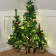 Sæt med tre kunstige juletræer med kogler, røde bær og varme hvide LED-lys. Træerne har baser indpakket i jutestof og gaveæsker under.