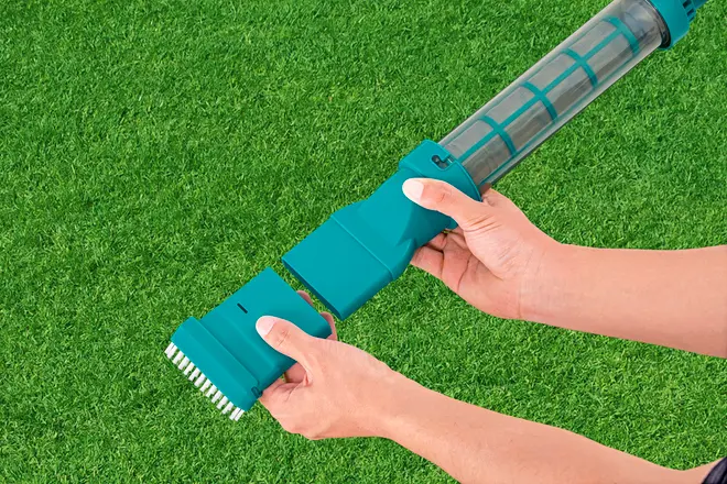 Håndholdt poolstøvsuger med aftageligt børstehoved, gennemsigtig filterbeholder og ergonomisk greb. Velegnet til nem rengøring af pools eller spa, vist på grøn græsbaggrund.