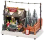 Miniatyr julgransmarknad med snö, figurer, trähus, ljusslinga och olika snötäckta granar. Inkluderar prislista och orange staket. Dekorativt tillbehör till julby.