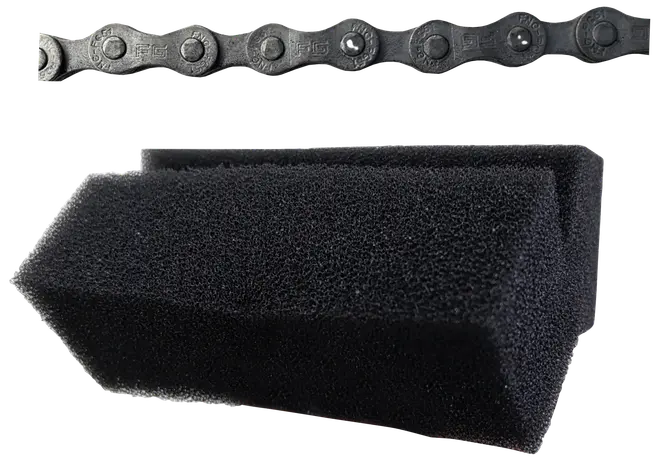 Sort rengøringssvamp med V-formet rille, designet til rengøring af cykelkæder. Billedet viser også et close-up af en cykelkæde over svampen.