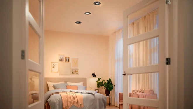 Moderne soveværelse med tre indbyggede loftspots, dobbelte glasdøre, lyse vægge, hyggelig seng med pastelfarvet sengetøj, vægkunst, potteplante og lyse gardiner for varm stemning.