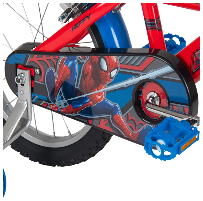 Nærbillede af en rød børnecykel med Spider-Man kædeskærm, blå pedal, baghjul og sølvfarvet støttehjul.
