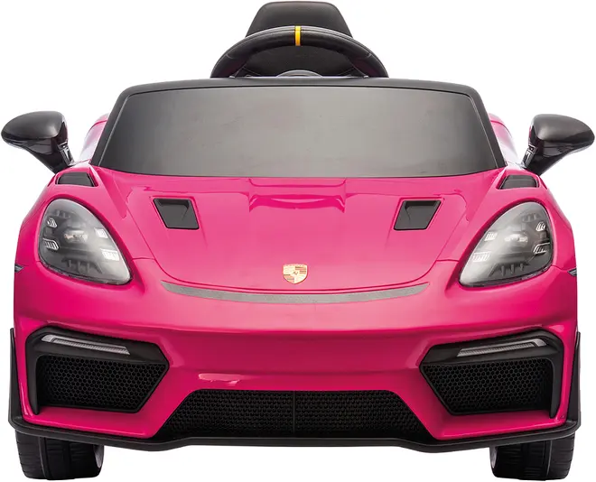 Lyserød elbil til børn, designet som en sportsvogn med realistiske forlygter, sort kølergrill, sidespejle og rat. Porsche-logo på motorhjelmen.