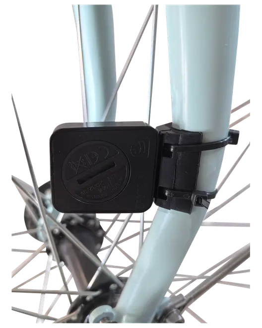 Sort plastiksensor monteret på en lyseblå cykelgaffel med strips, placeret tæt på egerne til registrering af cykeldata. Kompakt, vejrbestandigt design til udendørs brug.