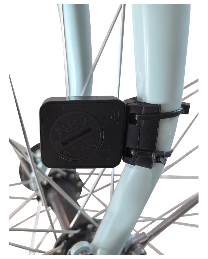 Sort plastiksensor monteret på en lyseblå cykelgaffel med strips, placeret tæt på egerne til registrering af cykeldata. Kompakt, vejrbestandigt design til udendørs brug.