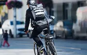 Stor sort og grå rygsæk med reflekterende striber, båret af cyklist. Har flere rum, justerbare stropper og vandafvisende materiale, ideel til pendling eller udendørs brug.