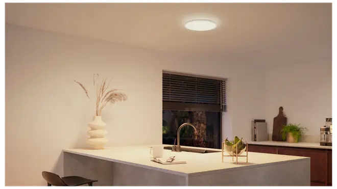 Moderne køkken med rund, indbygget LED-loftlampe. Hvid køkkenø med vask, minimalistisk dekoration og trædetaljer. Lampen giver klart, jævnt lys.