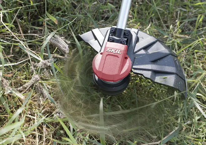 SKIL græstrimmer med rød og sort hoved, beskyttelsesskjold og roterende snøre, ideel til trimning af græs og ukrudt udendørs.