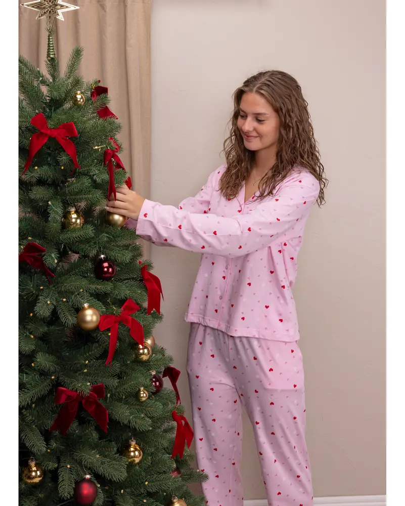 Ljusrosa pyjamaset med långärmad tröja och byxor, dekorerat med små röda hjärtan. Tillverkat av mjukt tyg, perfekt för vila eller sömn, visas på kvinna.