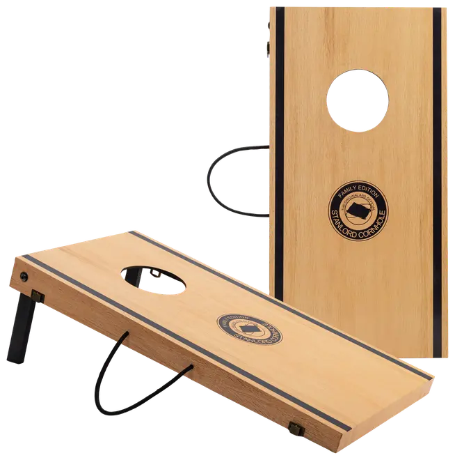 Sæt med to cornhole-brætter i træ med rundt hul, foldbare sorte ben, bærehåndtag og centralt logo med teksten 'Family Edition Standard Cornhole.' Naturtræ med sorte detaljer.