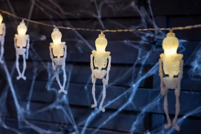Ljusslinga med lysande skelettfigurer, varje figur hänger från en tråd. Perfekt för Halloween, vita plastskelett med upplysta huvuden mot mörk bakgrund med spindelväv.