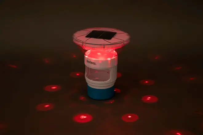 Solcelledrevet flydende poollys med rund top, hvid og blå krop, udsender røde LED-lys i cirkler. Velegnet til pooldekoration og aftenstemning.