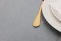 Elegant dukning med guldfärgad kniv, vita tallrikar och vit tygservett på ljusgrå duk. Modern, minimalistisk stil för formella middagar.