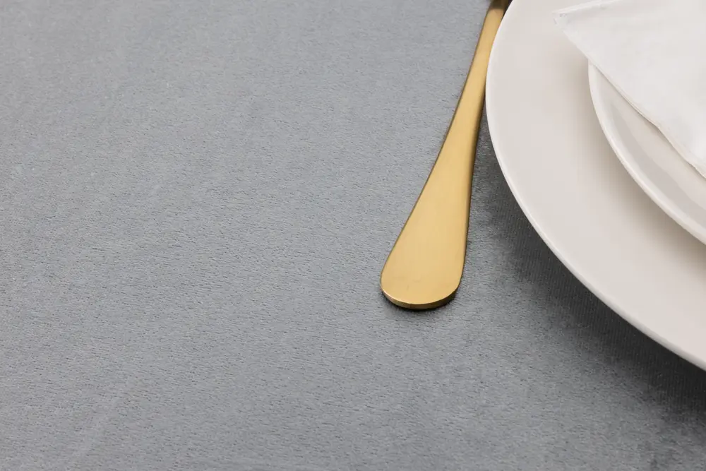 Elegant dukning med guldfärgad kniv, vita tallrikar och vit tygservett på ljusgrå duk. Modern, minimalistisk stil för formella middagar.