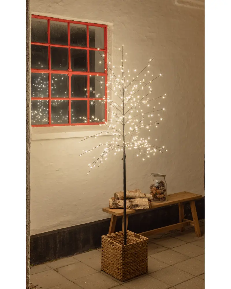 Konstgjort träd med varmvita LED-lampor på nakna grenar, placerat i en flätad korg. Passar för inomhus- eller skyddad utomhusdekoration, ger mysig stämning.