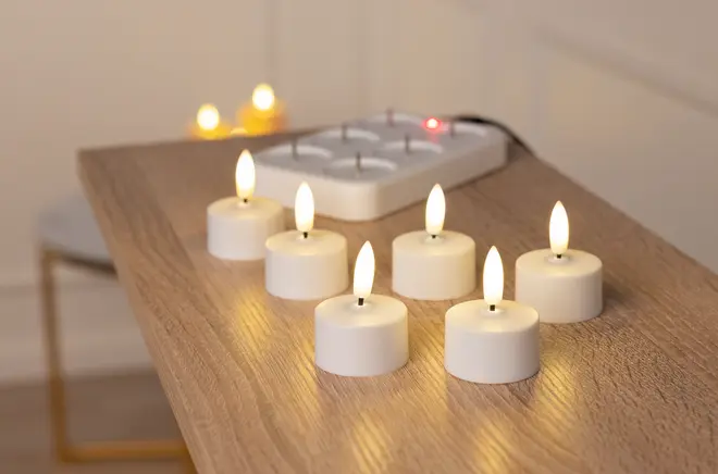 Sæt med seks batteridrevne LED fyrfadslys med hvide baser og realistisk flammeeffekt, placeret på en træoverflade. Sikker dekoration eller stemningsbelysning.