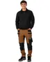 Herrarbetsbyxor i brunt och svart med flera fickor, förstärkta knän och verktygsslingor. Slitstarkt tyg, för tuffa jobb. Visas med svart sweatshirt och sneakers.