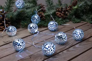 Ljusslinga med små silverfärgade discokulor, reflekterande mosaikmönster, perfekt för festlig dekoration. Visas på träyta med grankvistar och kottar i bakgrunden.