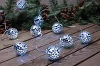 Ljusslinga med små silverfärgade discokulor, reflekterande mosaikmönster, perfekt för festlig dekoration. Visas på träyta med grankvistar och kottar i bakgrunden.