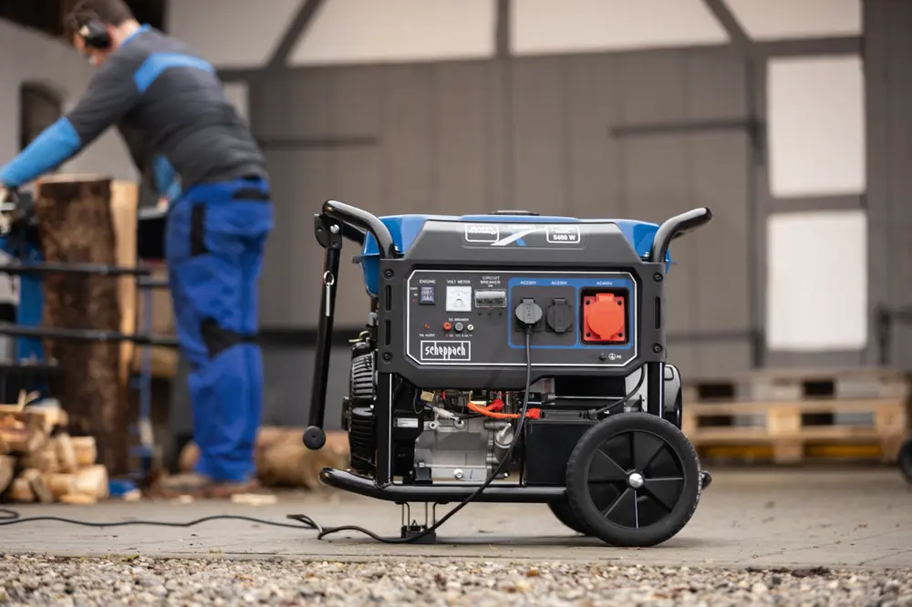 Bærbar generator med hjul og håndtag, flere strømudtag, kontrolpanel og robust ramme. Velegnet til udendørs eller nødbrug, vist i et værkstedsmiljø.