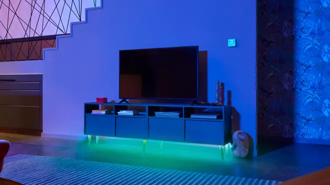 Moderne TV-bord med fire skuffer og åbne hylder, sort finish, LED-lys under i grøn, fladskærms-TV ovenpå. Dekorative genstande og bøger på hylderne.