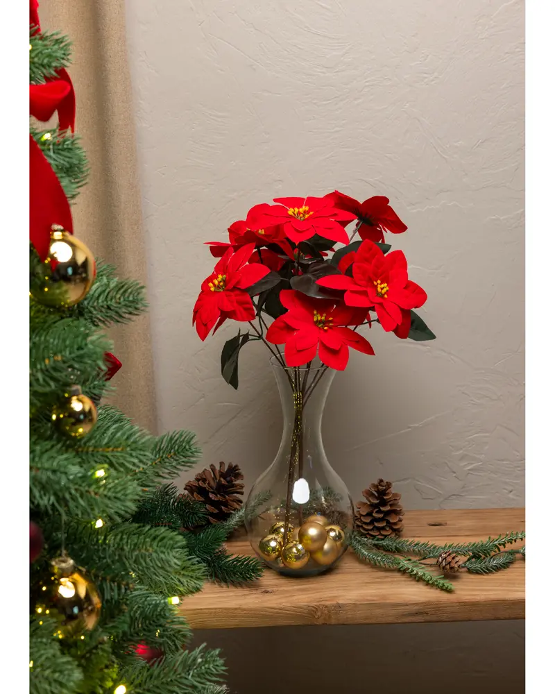 Konstgjorda julstjärnor med röda blad och gröna blad i en klar glasvas, dekorerad med guldfärgade kulor. Perfekt som festlig dekoration eller bordsdekoration.