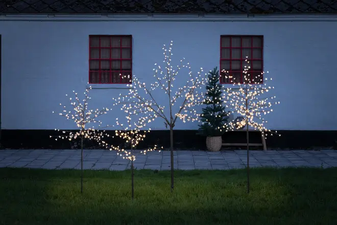 Set med tre konstgjorda utomhusträd med varmvita LED-lampor på grenarna, metallstavar för markplacering, passar till trädgårds- eller altandekoration, ger en festlig ljuseffekt.