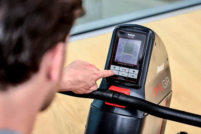 Reebok ONE GR romaskine med digitalt display, kontrolknapper og solidt håndtag. Brugeren betjener konsollen, som viser træningsdata og programmuligheder for effektiv træning.