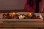 Rektangulär vit bricka med tre LED-värmeljus formade som pumpor och en dödskalle, omgivna av torkade löv och grön mossa, perfekt för Halloween-dekoration.